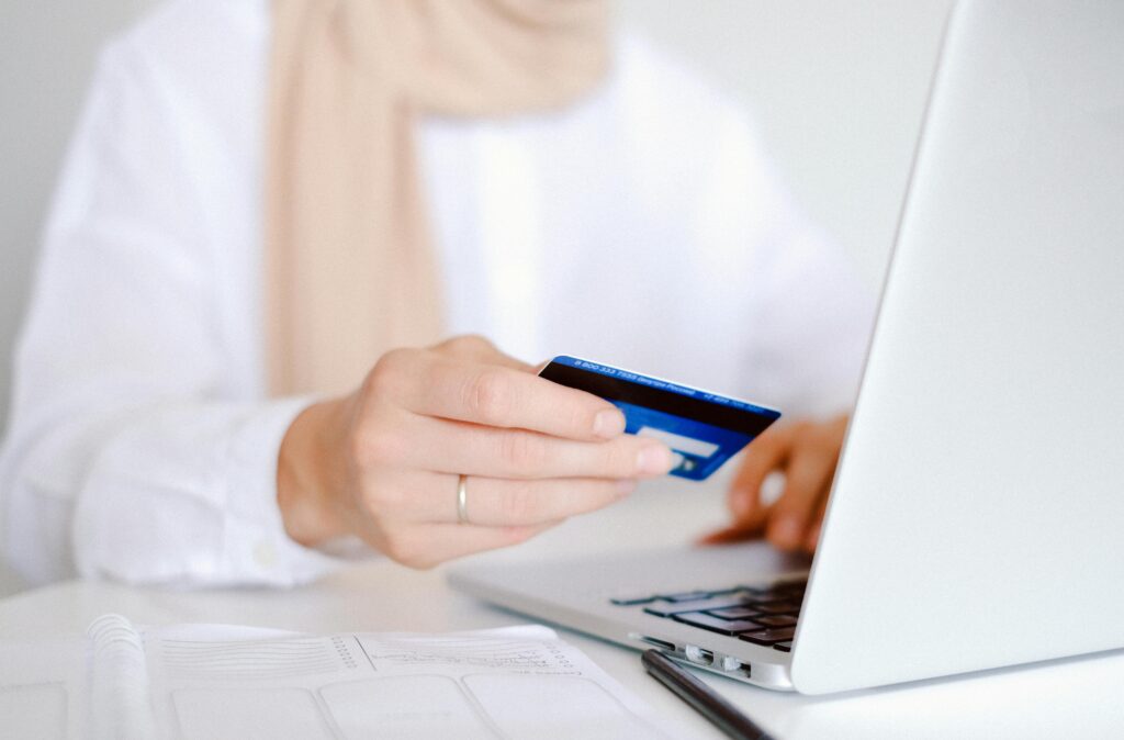 Close-up of a person holding a credit card while using a laptop for online shopping.